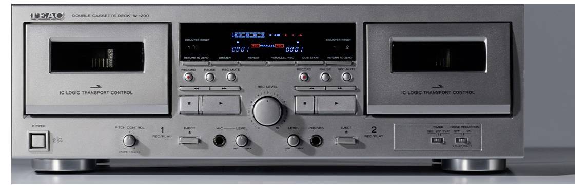 Pogled sprijeda srebrnog stereo kasetofona s dva pretinca za kasete, centralnim digitalnim zaslonom, tipkama, gumbima i kontrolama prijenosa.