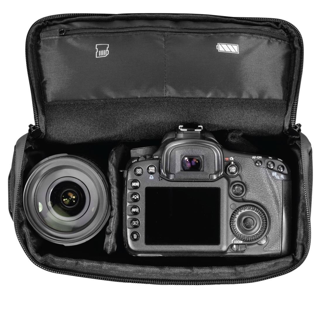 Otvorena kamera torba s tijelom DSLR-a i odvojenom lećom, snimljena odozgo na bijeloj pozadini.