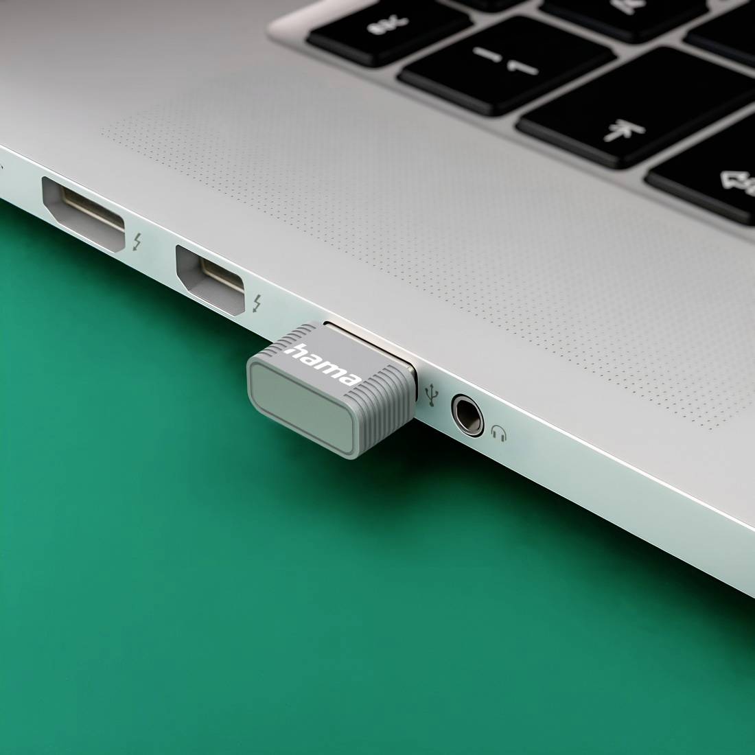 Detaljan prikaz bočne strane laptopa s priključenim USB-C adapterom u priključak, prikazujući obližnje USB i slušalice na zelenoj površini.