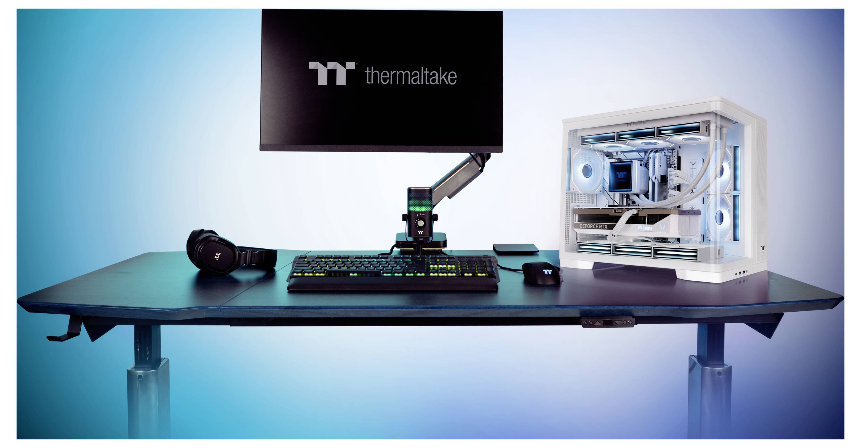 Postavka za igranje s Thermaltake monitorom, RGB tipkovnicom i mišem, slušalicama, krakom za mikrofon i bijelom prilagođenom PC kućištem s plavim osvjetljenim ventilatorima.