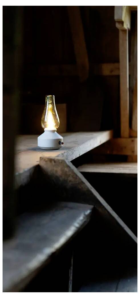 Mala, upaljenja lampa sjedi na drvenom nosaču u tamnoj, rustikalnoj unutrašnjosti.