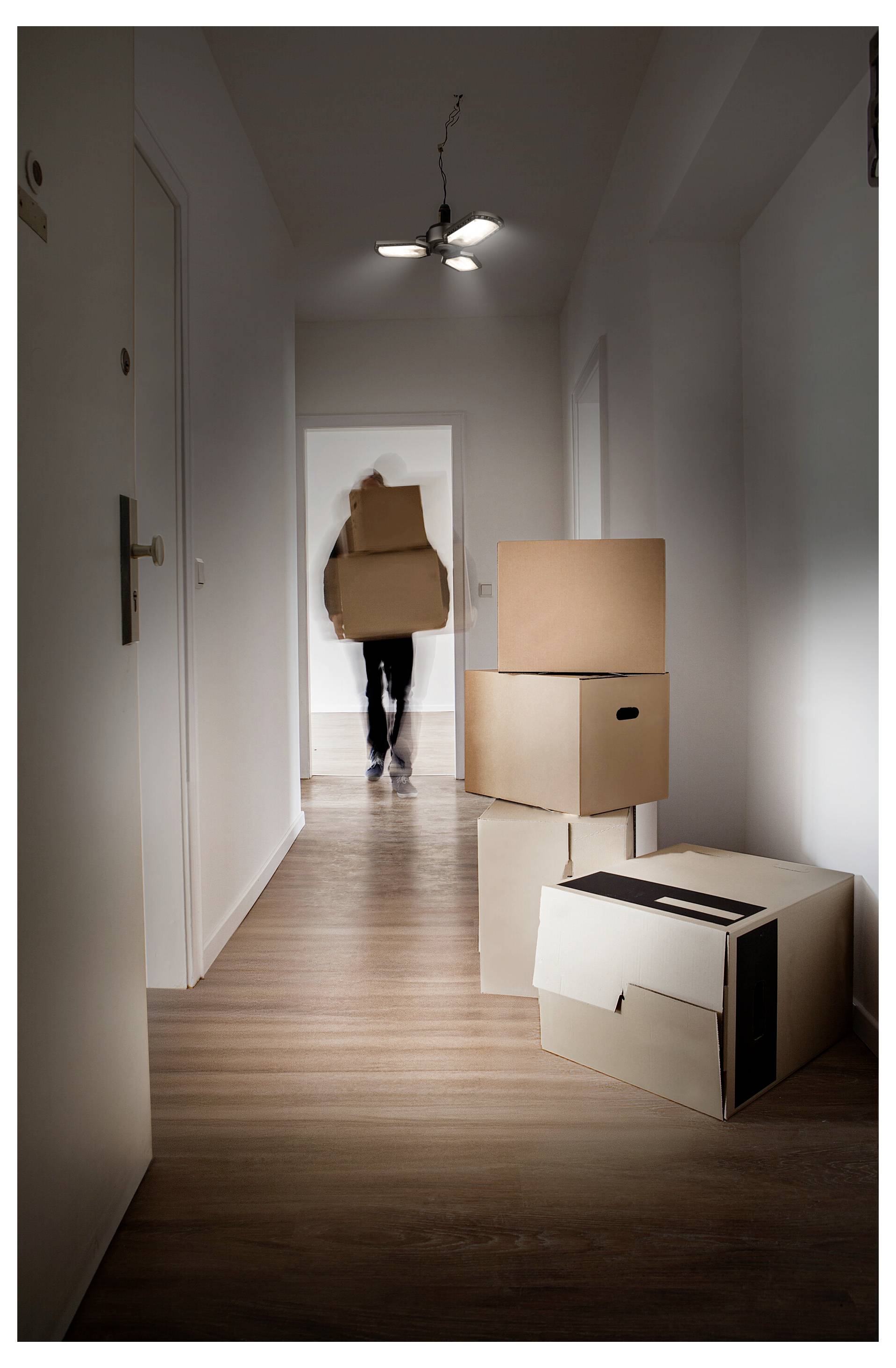 Osoba koja nosi kutije za selidbu niz hodnik u praznom stanu, s nekoliko zapakovanих kutija naslaganih u prvom planu.