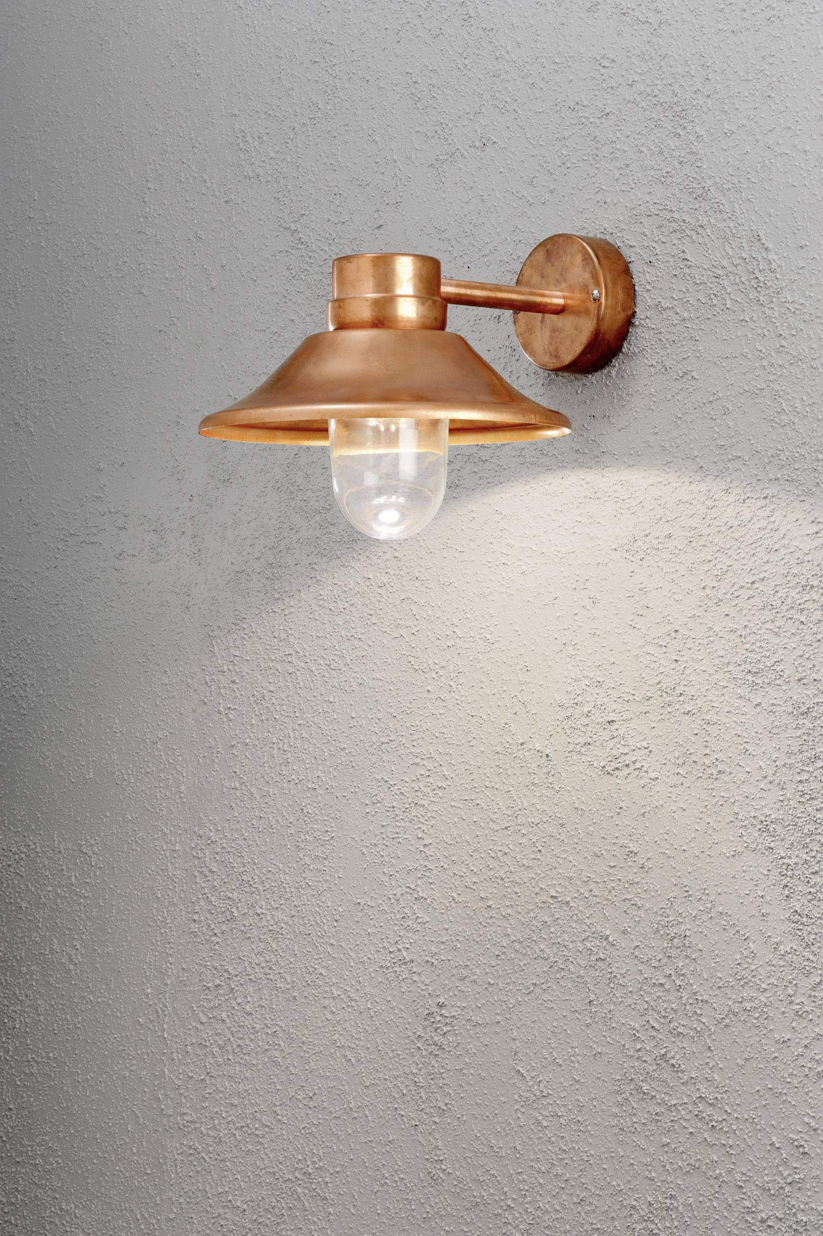 Viseća zidna lampa od bakra osvjetljava sivi strukturirani zid. Minimalistički dizajn s toplim osvjetljenjem.