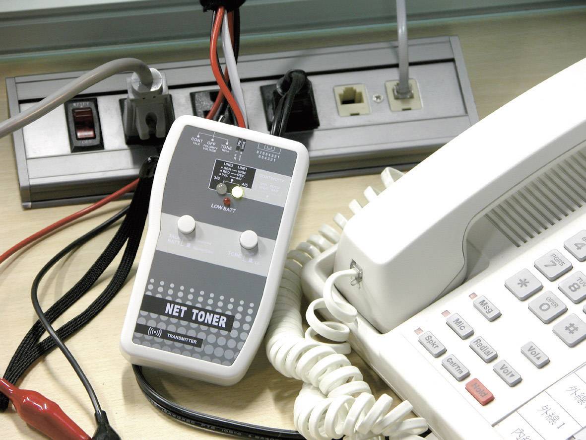 Telefon i mrežni adapter na radnom stolu, okruženi kabelima i utičnicama, prikazuju postavljanje za tehničko održavanje ili instalaciju.