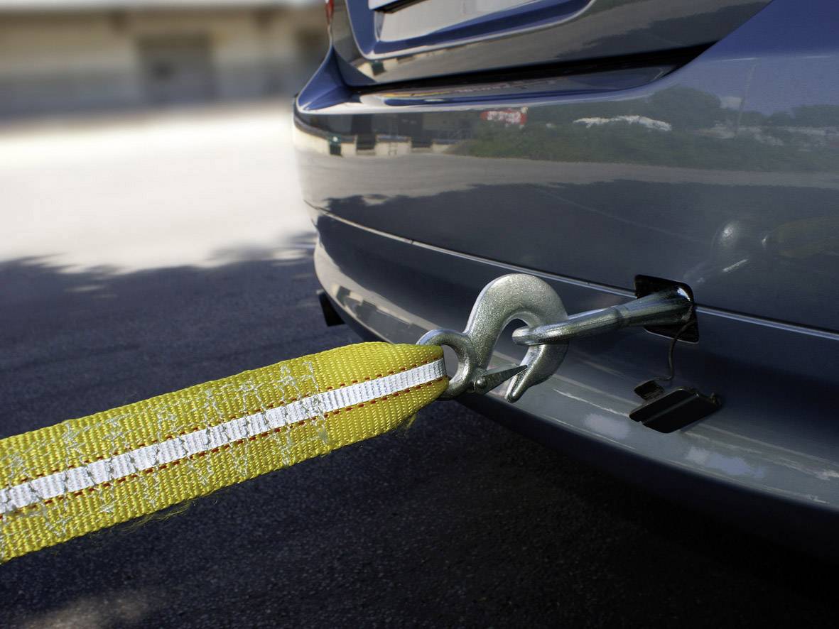 Žuti trakasti vučni pojas pričvršćen je za kuku na stražnjem dijelu automobila. Pojas je zateznog i spreman za vuču.