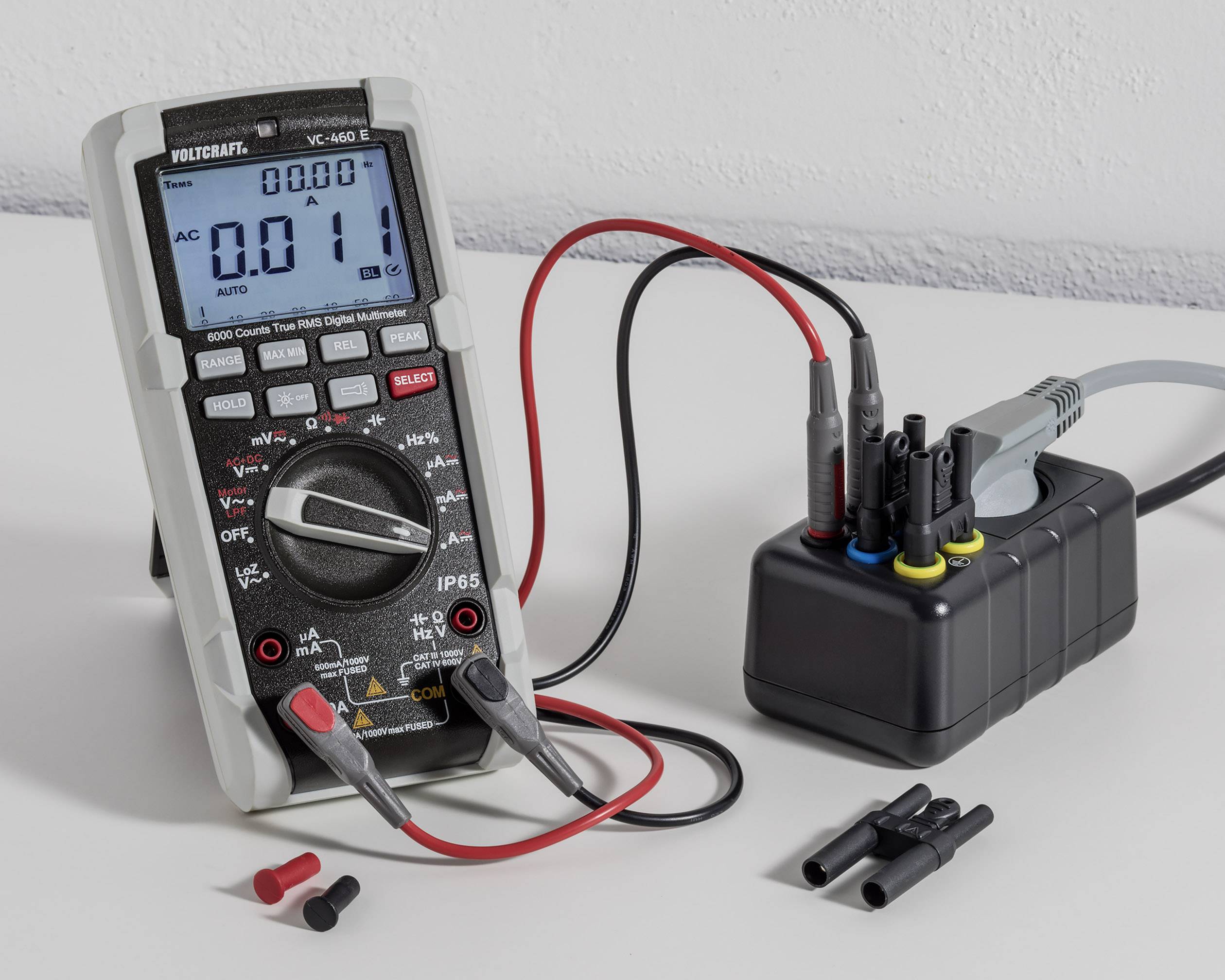 Digitalni multimetar i spojni kablovi na stolu prikazuju napon od 0,11 V. Uređaj je spojen s obojenim utičnicama.