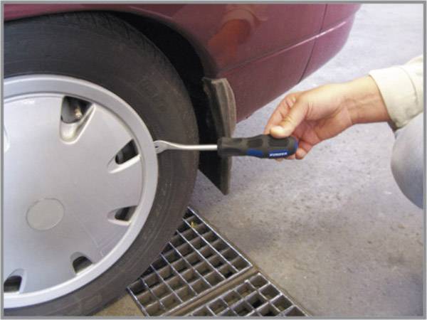 Jedna osoba koristi alat kako bi uklonila poklopac kotača automobila. Alat se uvlači između poklopca kotača i gume.