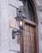 Vanjska metalna lampa, osvjetljena, postavljena na kamenom zidu pored drvenih vrata s željeznim okovima.
