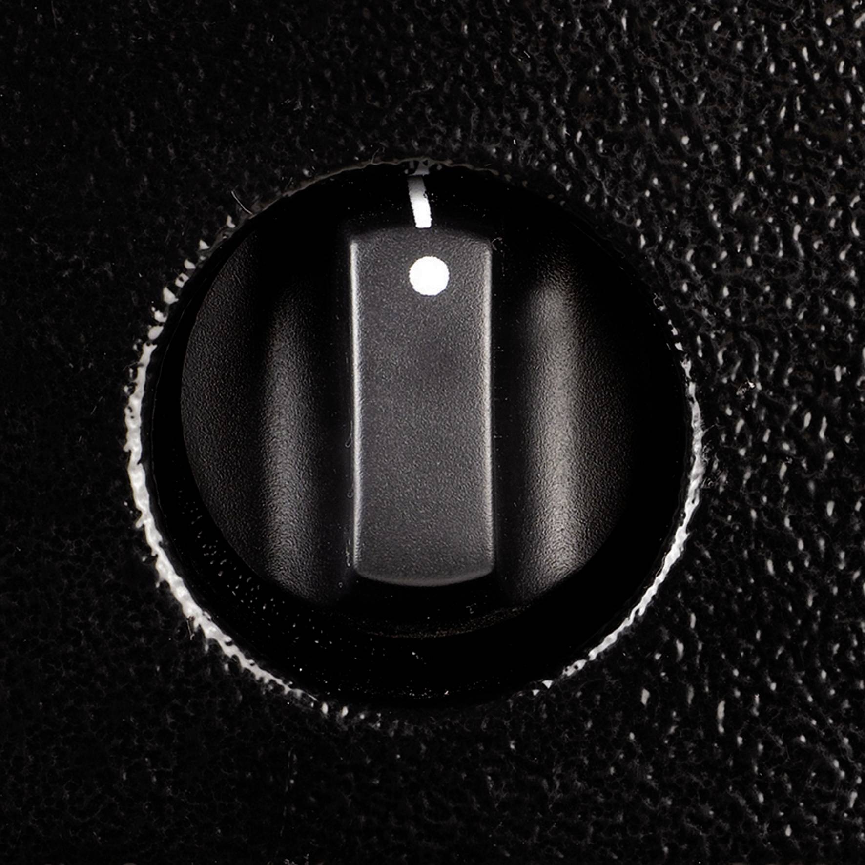 Crni plastični prekidač s bijelom točkom nalazi se u srednjem položaju na strukturiranoj crnoj površini.