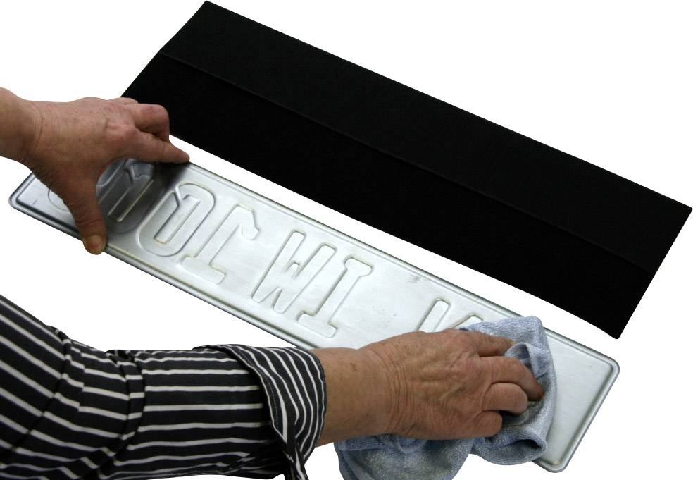 Jedna osoba čisti nemontirani registarski broj automobila plavom krpom. S lijeve strane je vidljiv crni nosač.