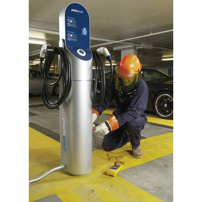 Tehničar u zaštitnoj opremi provjerava električni punjač automobila u podzemnoj garaži. Mjerni uređaj leži na podu.