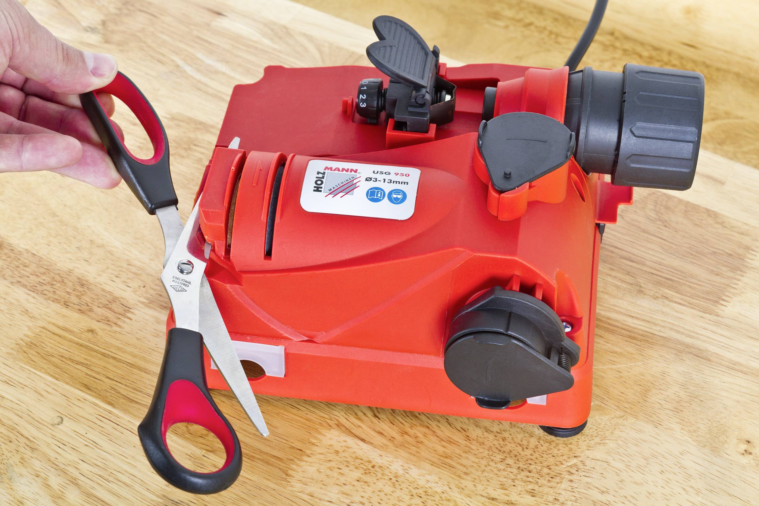 Crvena električna mašina za oštrenje koristi se za oštrenje škara. Jedna ruka drži škare na brušnom utoru.