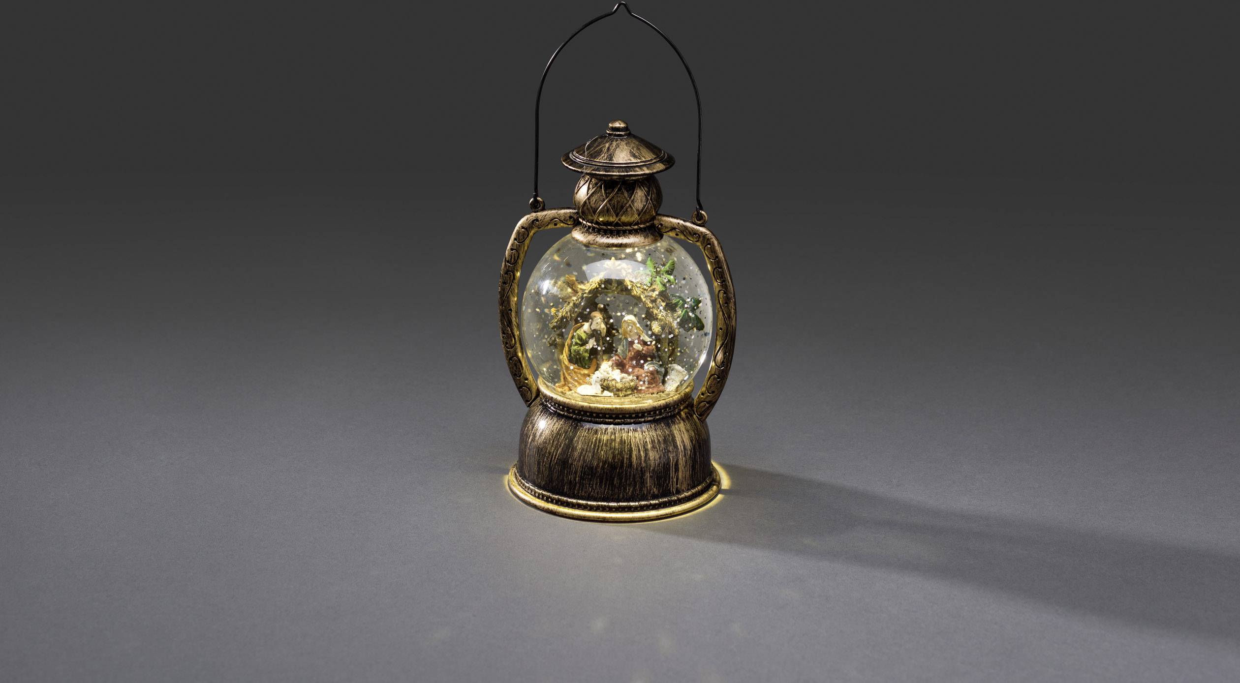 Antička lampa s zimskom krajolikom u unutrašnjosti, prikazuje figure, jelke i osvjetljenu kuću.