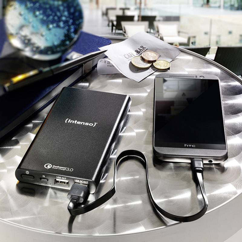 Powerbank tvrtke Intenso punjač je HTC pametni telefon na metalnom stolu, pored kojeg leže novčići i hrpa papira.