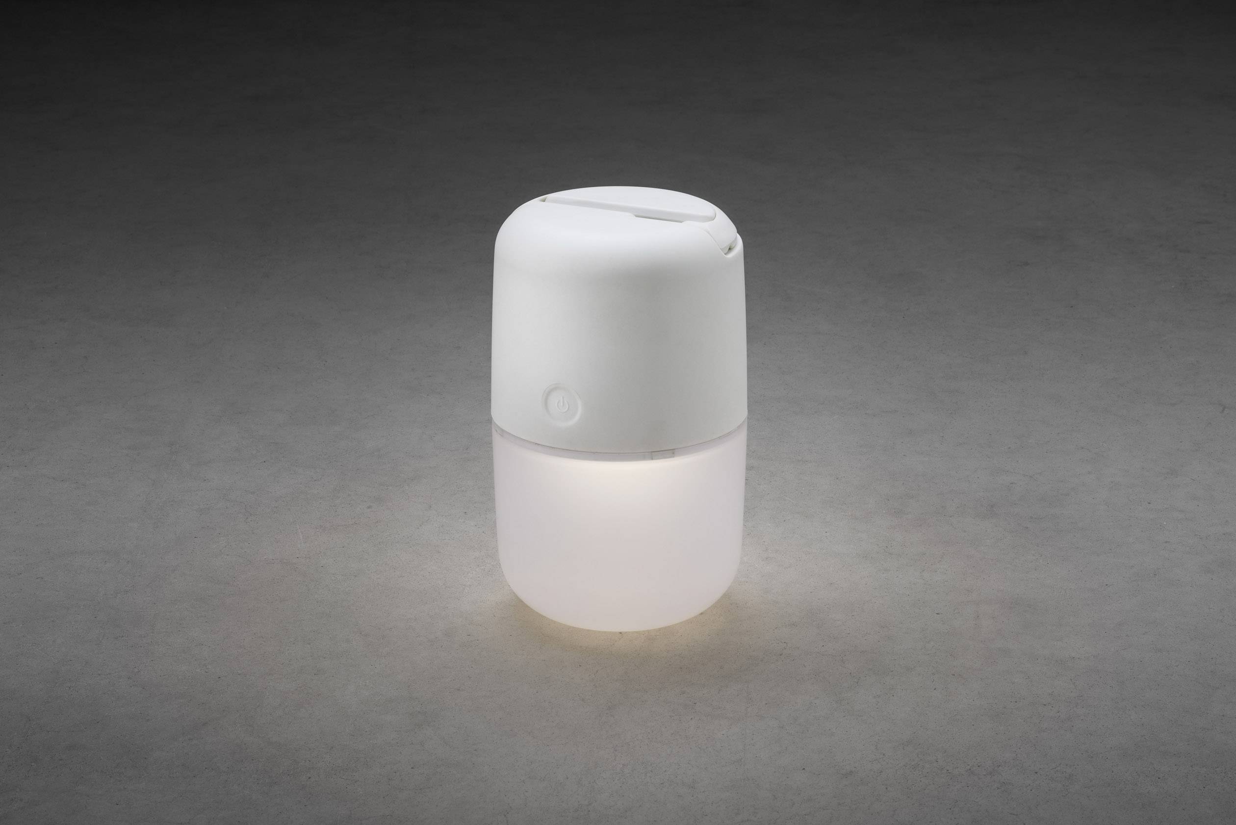 Bijeli, cilindrični ovlaživač zraka s nježno svijetlećom svjetlošću stoji na sivoj pozadini.