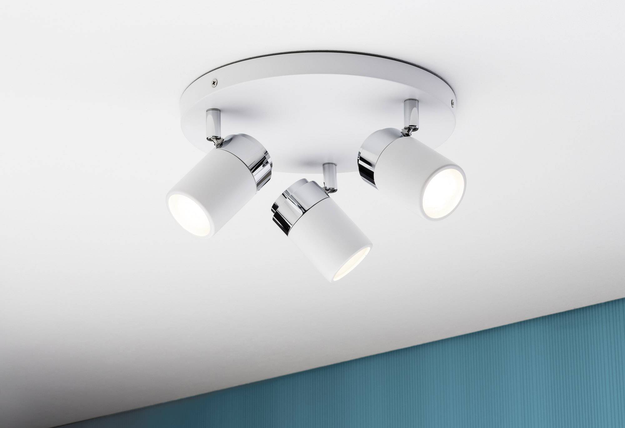 Stropna lampa s tri podesiva bijela reflektora na ovalnoj bazi pričvršćena na stropu sobe, vidljiv plavo obojani zid.