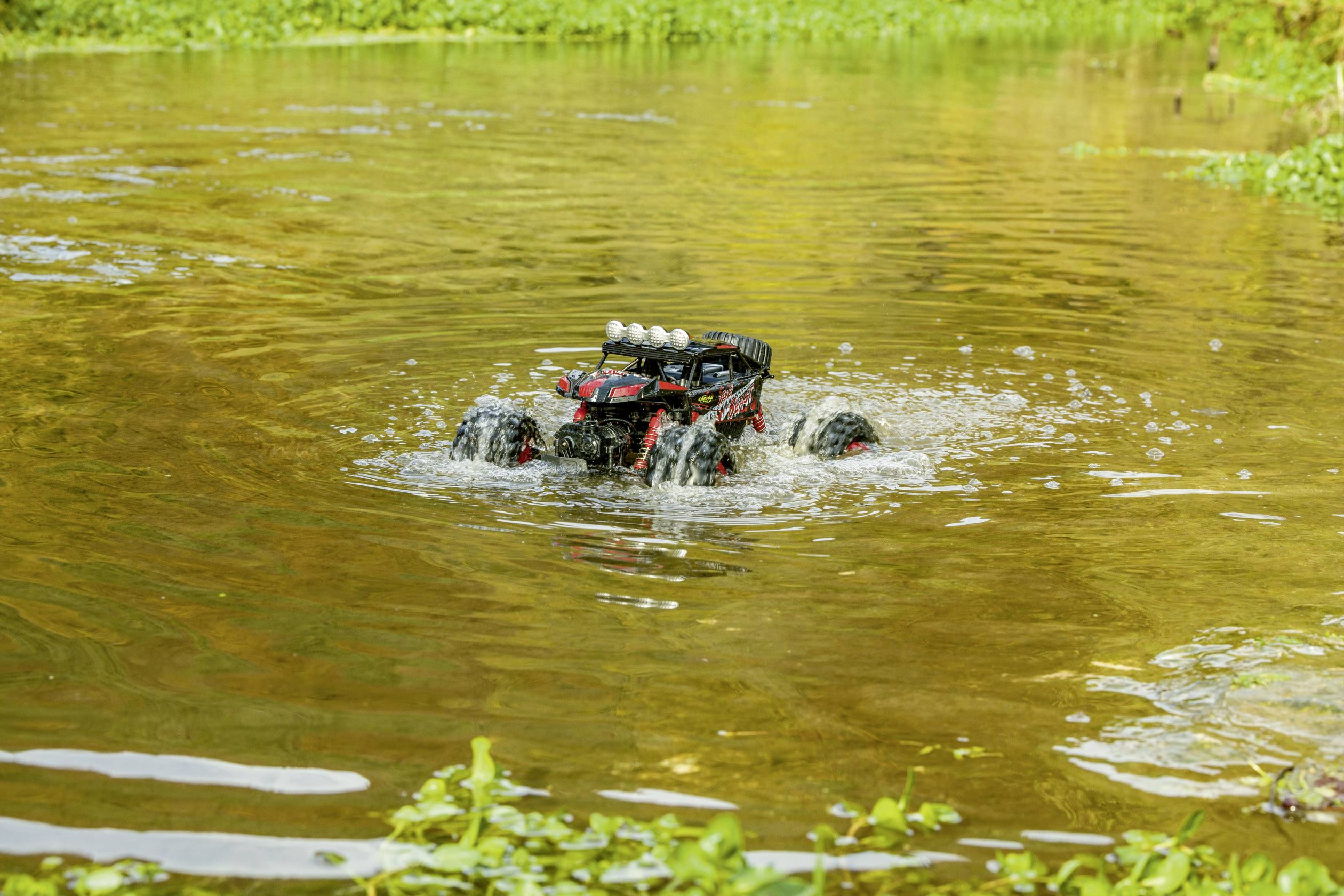 Daljinski upravljani automobil vozi kroz plitku vodu u nedirnuto prirodnom području. Prskanje vode ukazuje na kretanje.