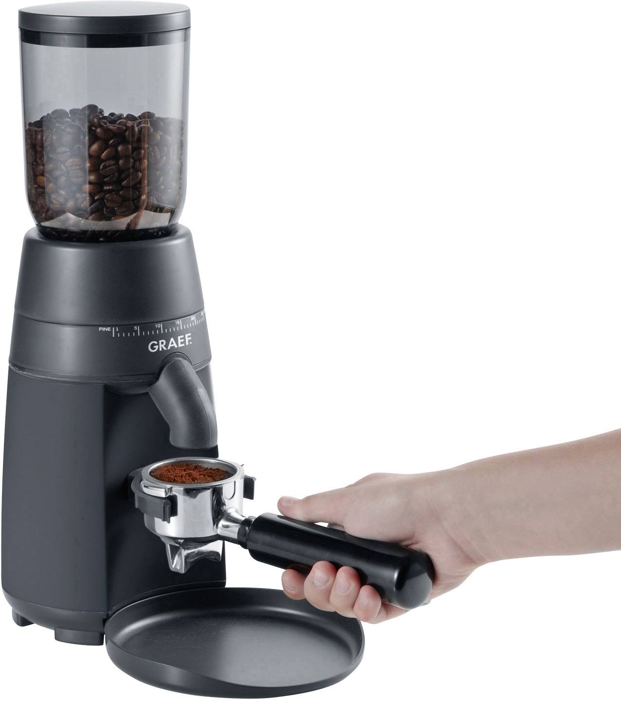 Jedna ruka drži filter za kavu ispod mlaznice električne kafeniske mlinice pune zrna kave.