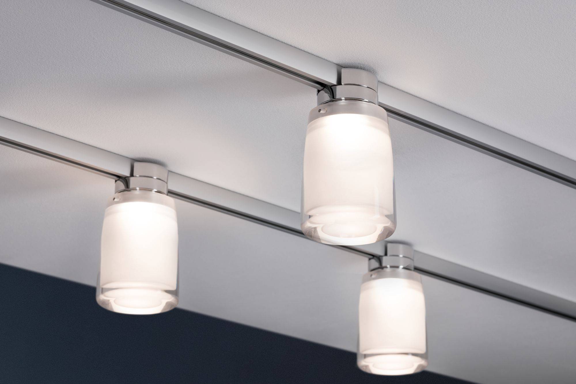 Tri moderne, cilindrične stropne lampe na metalnim tračnicama ravnomjerno osvjetljavaju prostor.