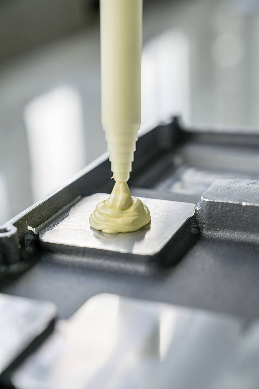 3D printer nanosi kremasto bijelu masu u slojevima na pravokutni komad metala.