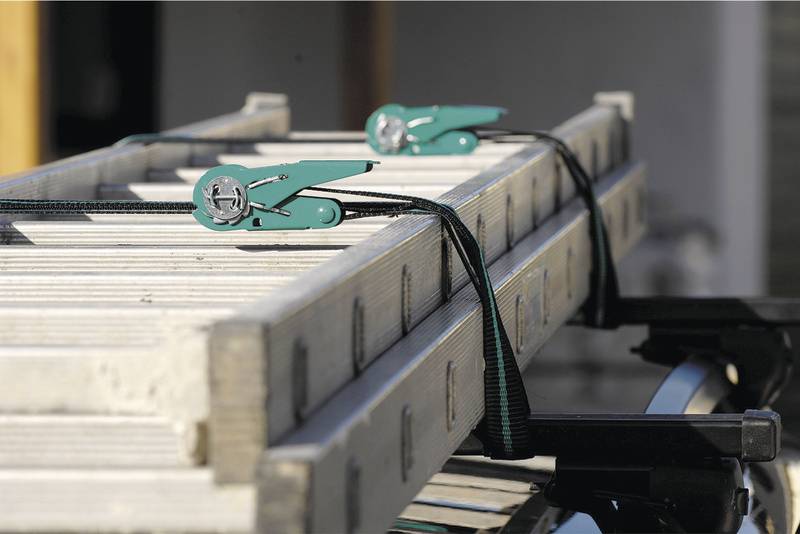 Metalni nosač učvršćen na krovu automobila, pričvršćen zateznim trakama i zelenim sigurnosnim kopčama, simbol transporta i sigurnosti.