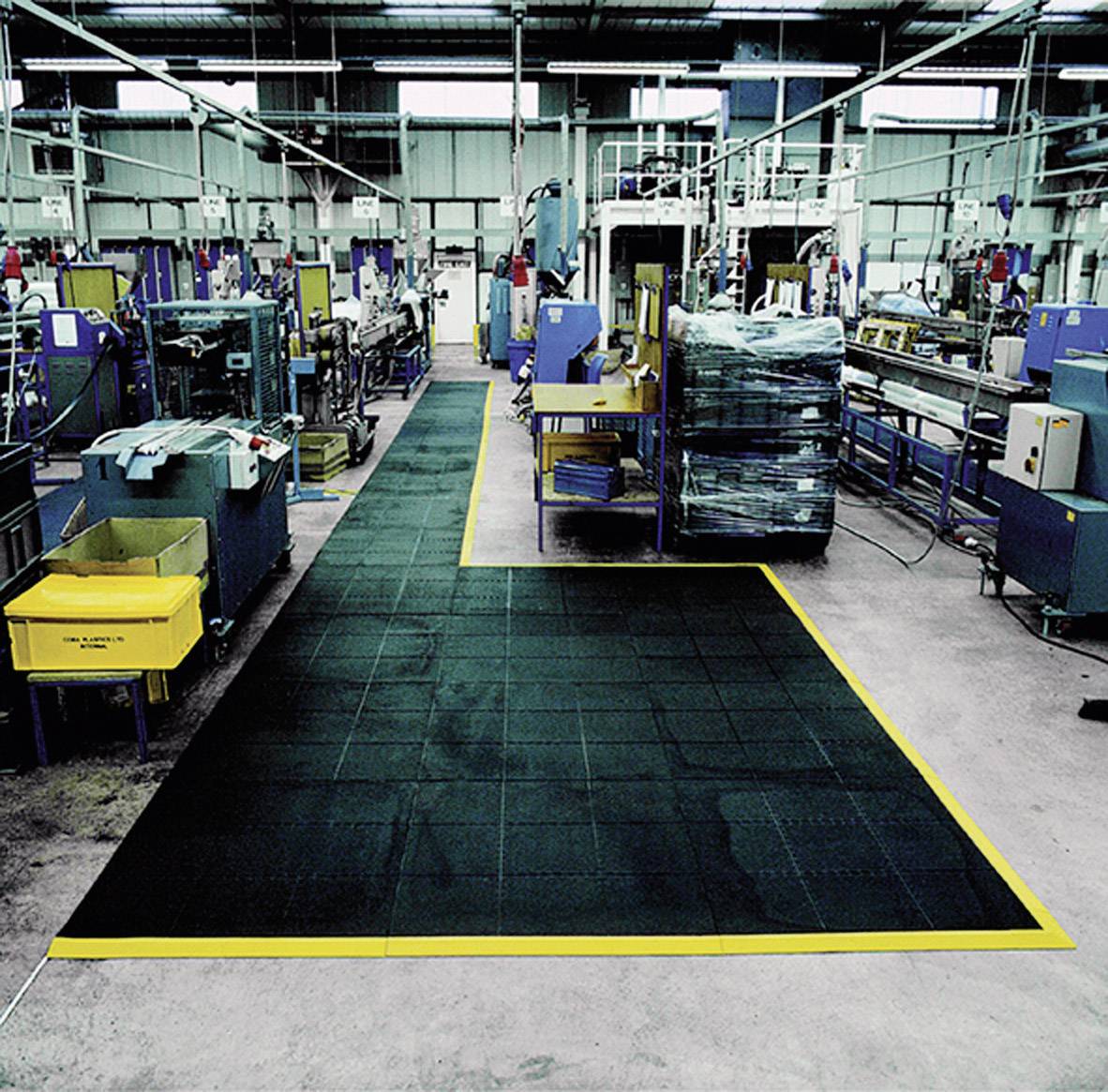 Velika industrijska hala s nizovima strojeva i označenom hodnicom od protukliznog materijala, zaštićena žutim oznakama.