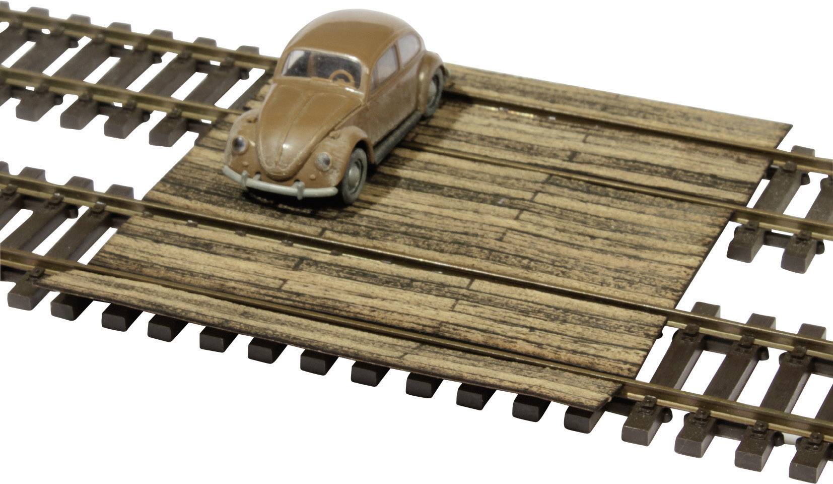 Svijetlosmeđi modelni automobil stoji na drvenom prijelazu željezničke pruge za igračke. Automobil izgleda nostalgično i klasično.