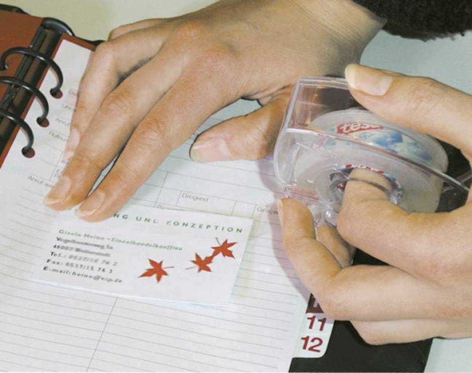 Jedna osoba koristi ljepljivu traku kako bi zalijepila posjetnice u bilježnicu. Kartica ima crvene zvijezde i kontakt informacije.