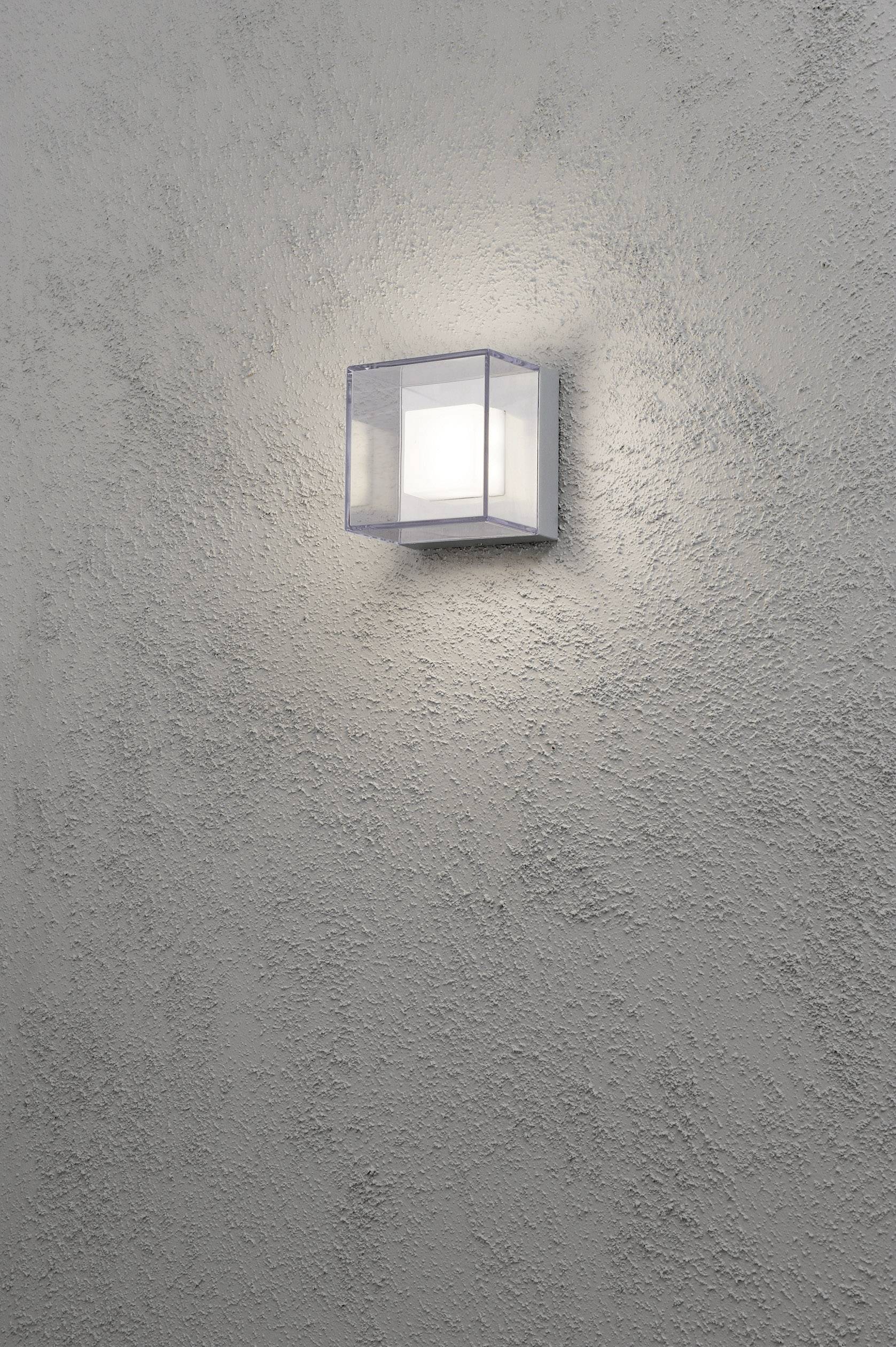 Zidna lampa u modernom, kvadratnom dizajnu nježno osvjetljava sivo strukturiranu stijenku, stvarajući minimalistički i elegantan ambijent.