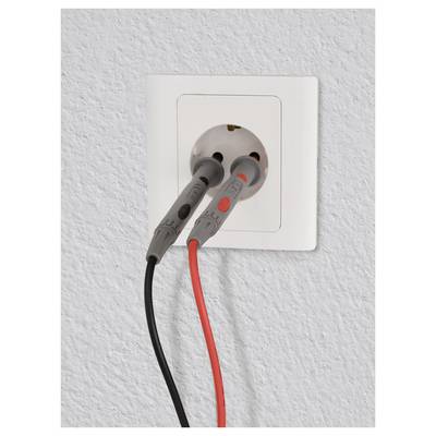 Elektromos aljzat két szondával, az egyik piros és a másik fekete, valószínűleg feszültségméréshez. Fehér fal háttérrel.