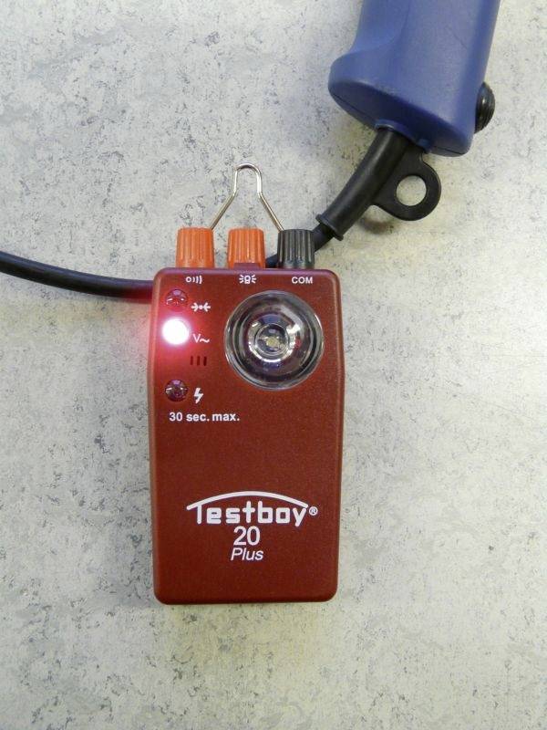 Piros elektromos tesztelőkészülék, 'Testboy 20 Plus', szürke háttérrel, világító piros LED-del és mérőhegyekkel.