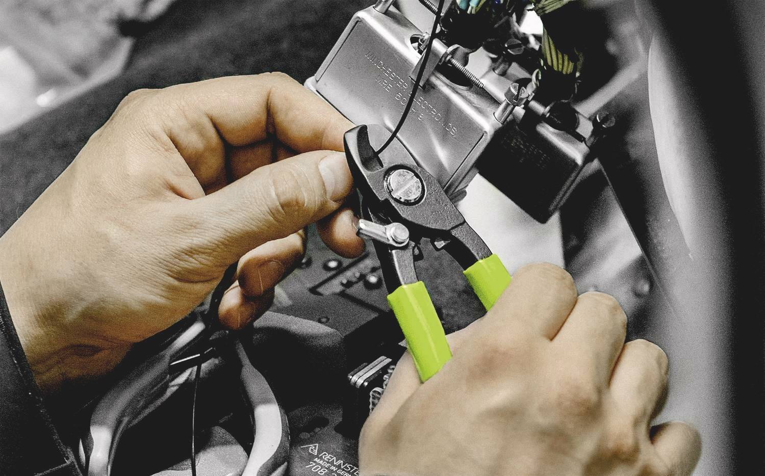 Egy személy fogja a kábelvágót és egy elektronikai eszköz bekábelezésén dolgozik.