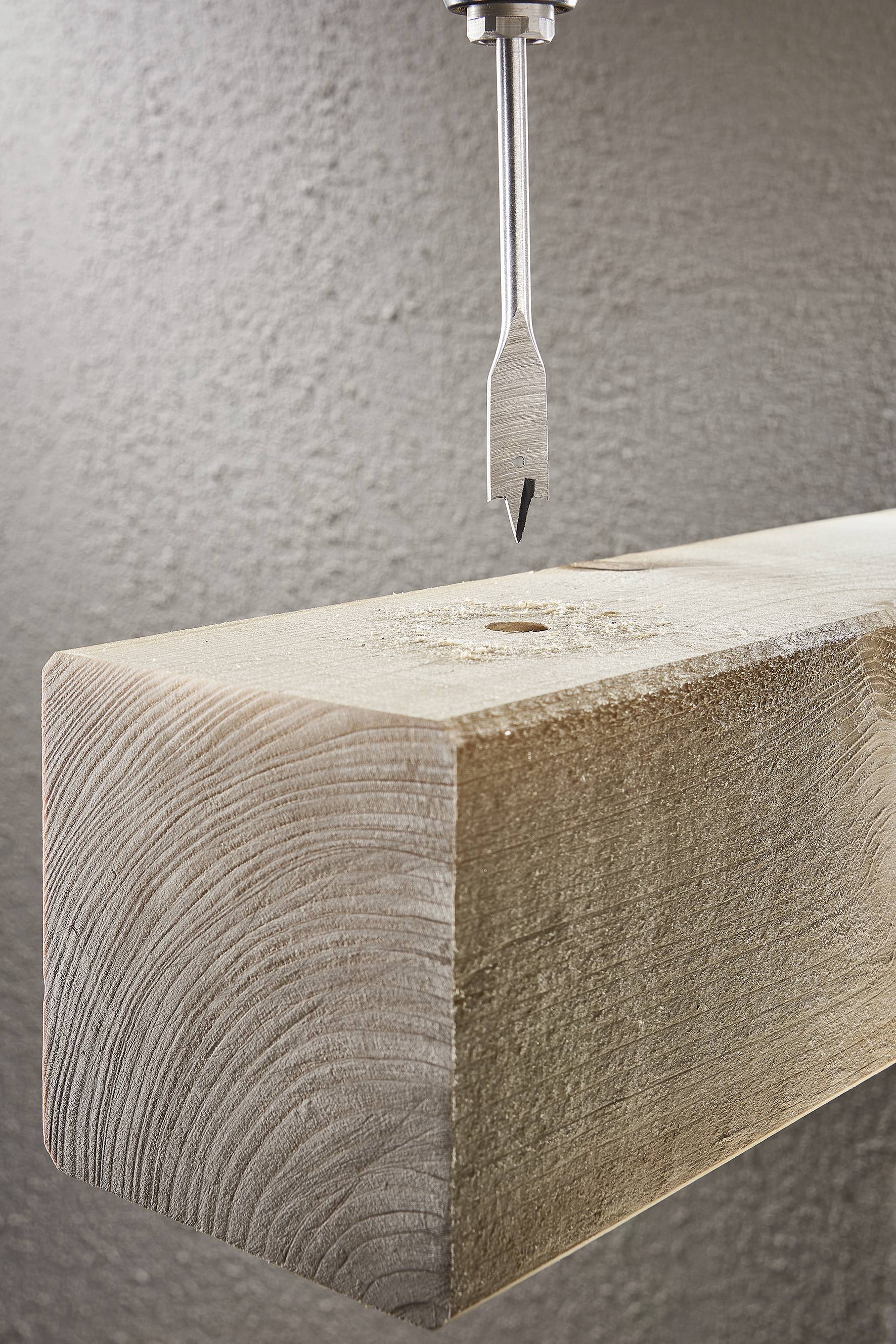 Egy fúrógép felülről közeledik egy fahasábhoz, készen arra, hogy lyukat fúrjon a fába.