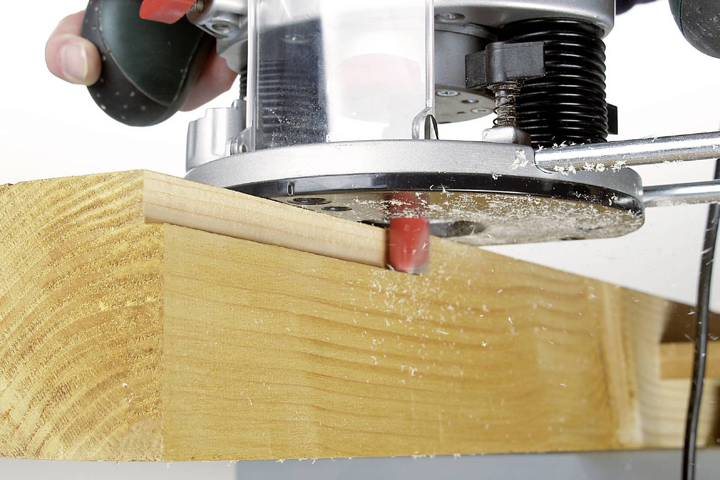 Egy kézi marógép megmunkálja egy fadarab szélét, sima felületet hoz létre és faforgácsokat termel.