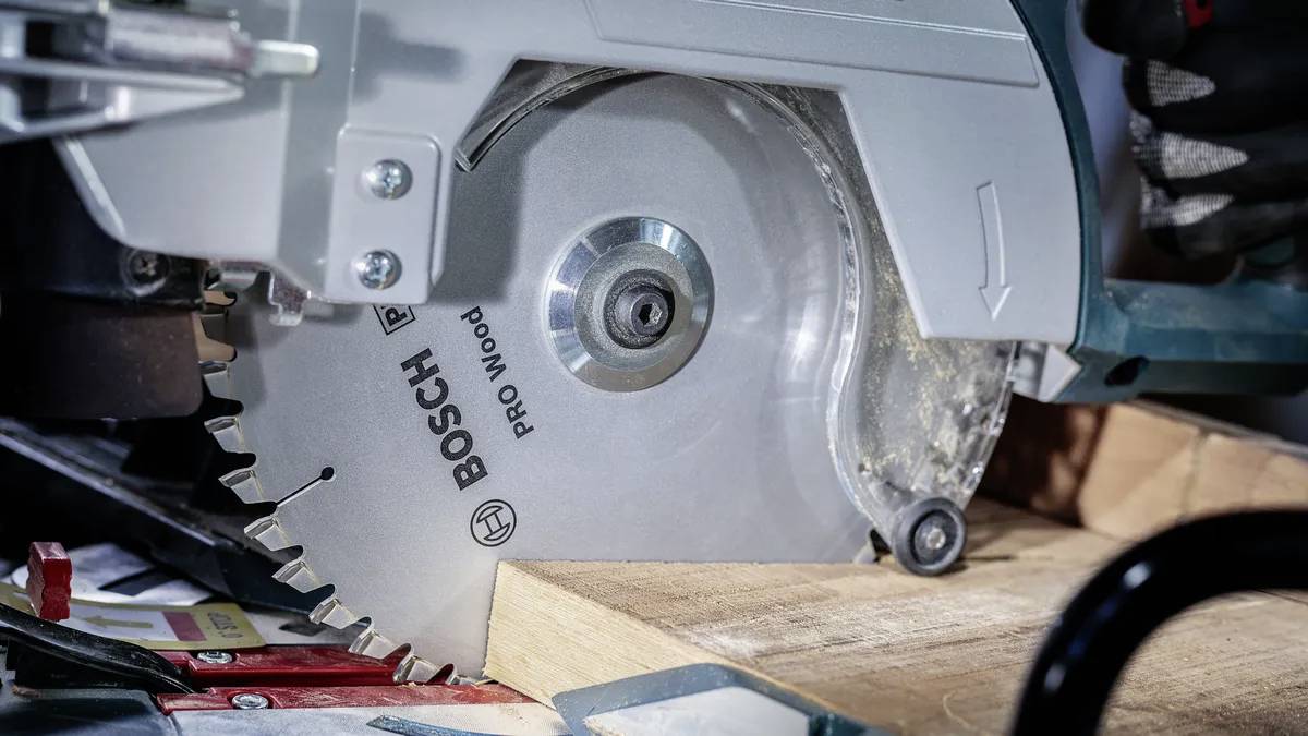 Egy körfűrész fűrészeli a fát, miközben látható a fűrészlap mozgása. A fűrész fémes felületű és a "BOSCH PRO Wood" feliratot viseli.