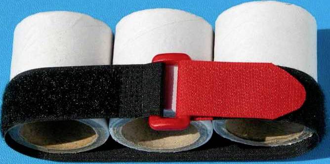 Három üres WC-papír tekercs egymás mellett, fekete tépőzárral összefogva, egy sima felületen fektetve.