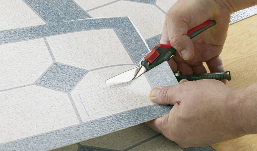 Kezek egy ollóval egy asztalon lévő csempemintát vágnak.