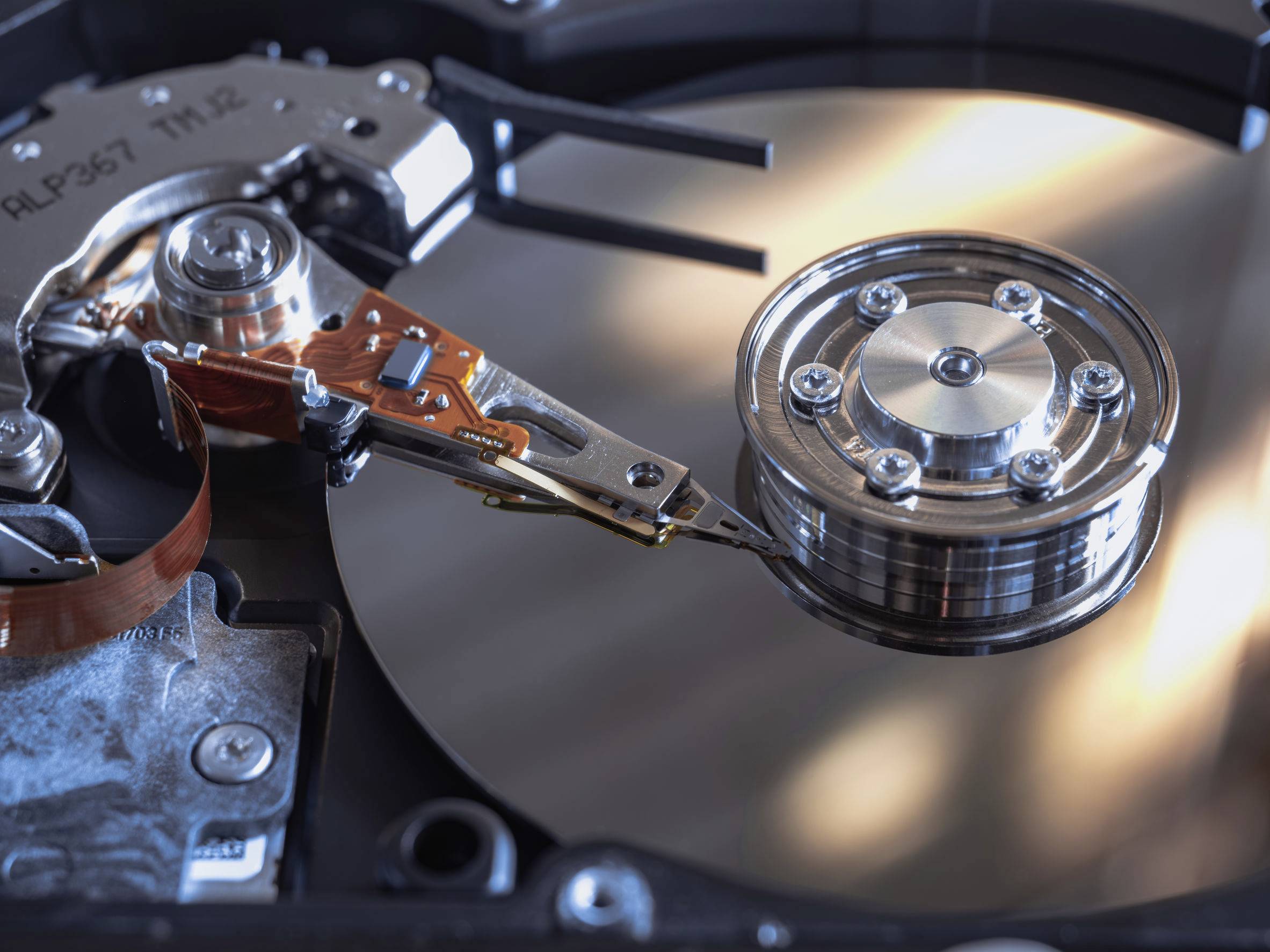Egy merevlemez-meghajtó közeli felvétele, amelyen látható a fénylő fémlemez és az adatelérést bemutató olvasó-író fej.