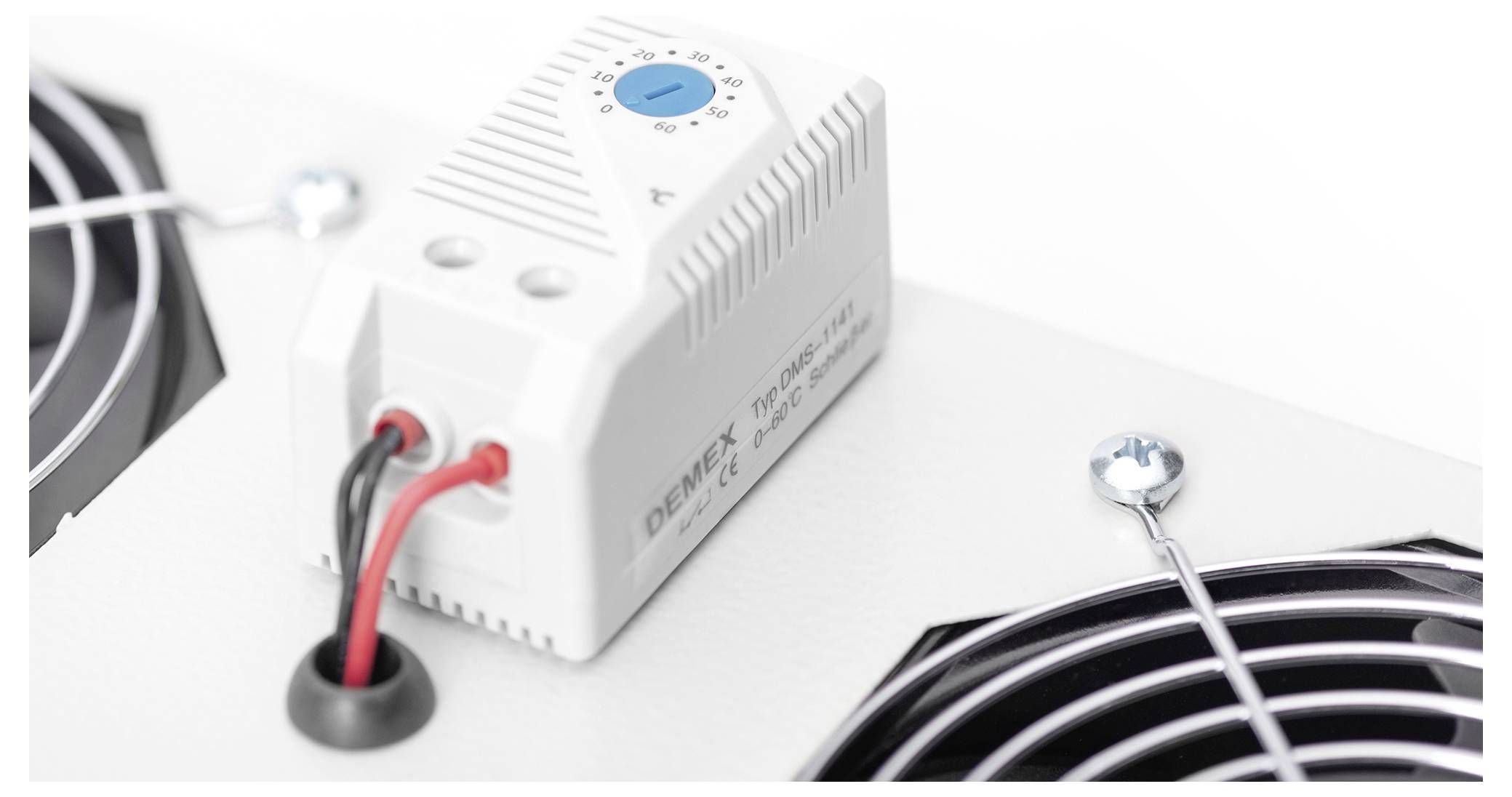Egy elektronikus eszköz közelképe, amely piros és fekete vezetékekkel van összekötve, két fém ventilátorszelep felett helyezkedik el fehér háttéren.