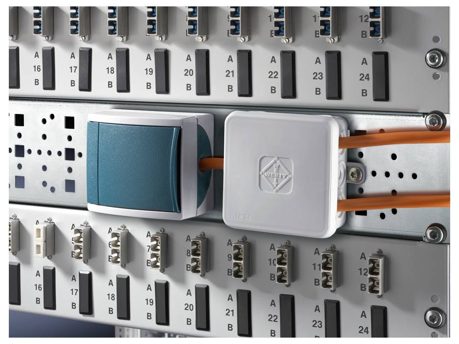 Egy kapcsolószekrény elektronikus csatlakozókkal, kábelekkel és csatlakozókkal. Egy zöld és egy szürke modul láthatóan be van dugva.