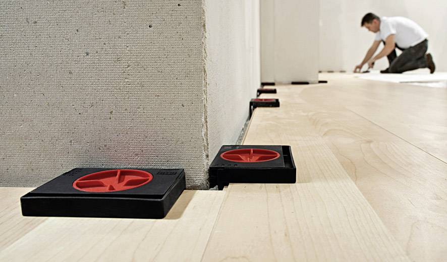 Egy férfi fapadlót fektet le. A falnál távtartók vannak elhelyezve, hogy biztosítsák a helyes fugaszélességet.