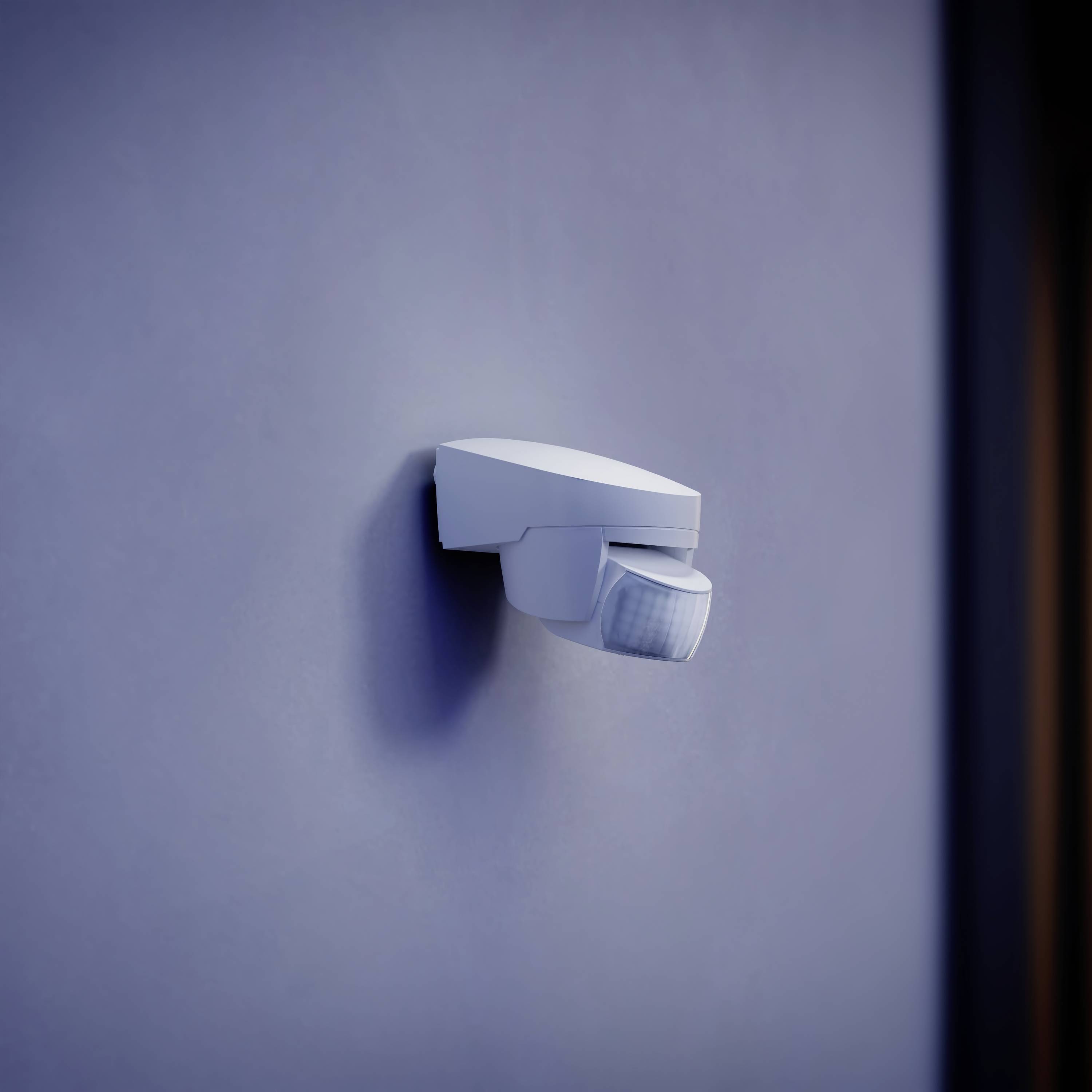 Egy fehér mozgásérzékelő egy kék falon, készen arra, hogy érzékelje a mozgásokat a helyiségben.