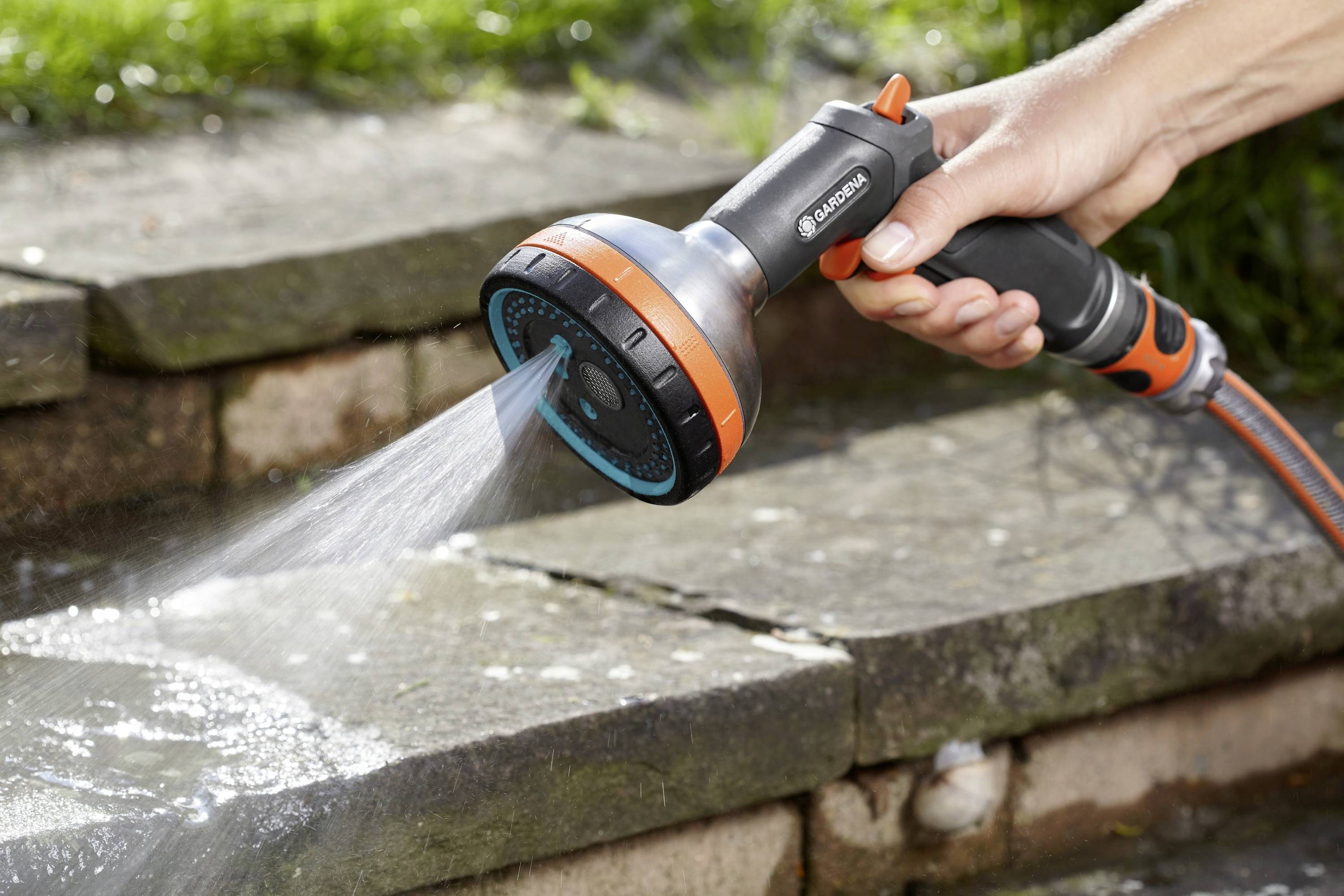 Egy kéz egy állítható kerti locsolófejjel öntöz egy kültéri kőlépcsősort.