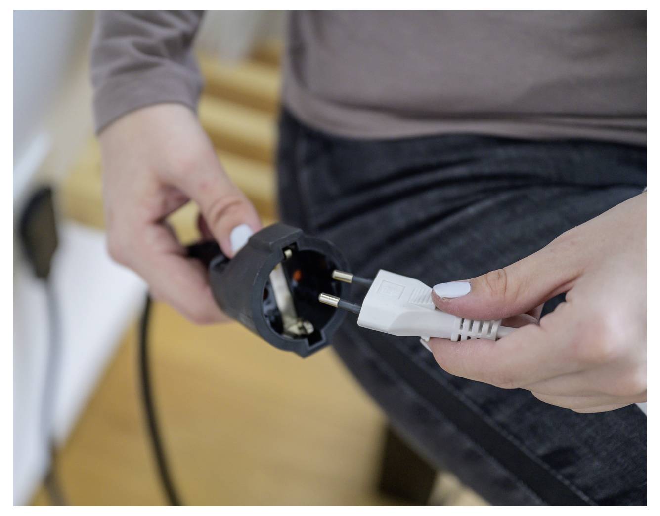 Egy személy fehér tápkábelt csatlakoztat egy fekete elektromos adapterbe vagy dugóba, amelyet mindkét kézben tart.