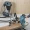 Egy körfűrész egy fadeszkát vág. A háttérben egy ipari porszívó látható. Mindkét eszköz egy fa padlón áll.