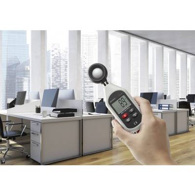 Egy kéz egy digitális hőmérőt tart egy modern irodában, amelynek hátterében íróasztalok, számítógépek és magas ablakok láthatók.