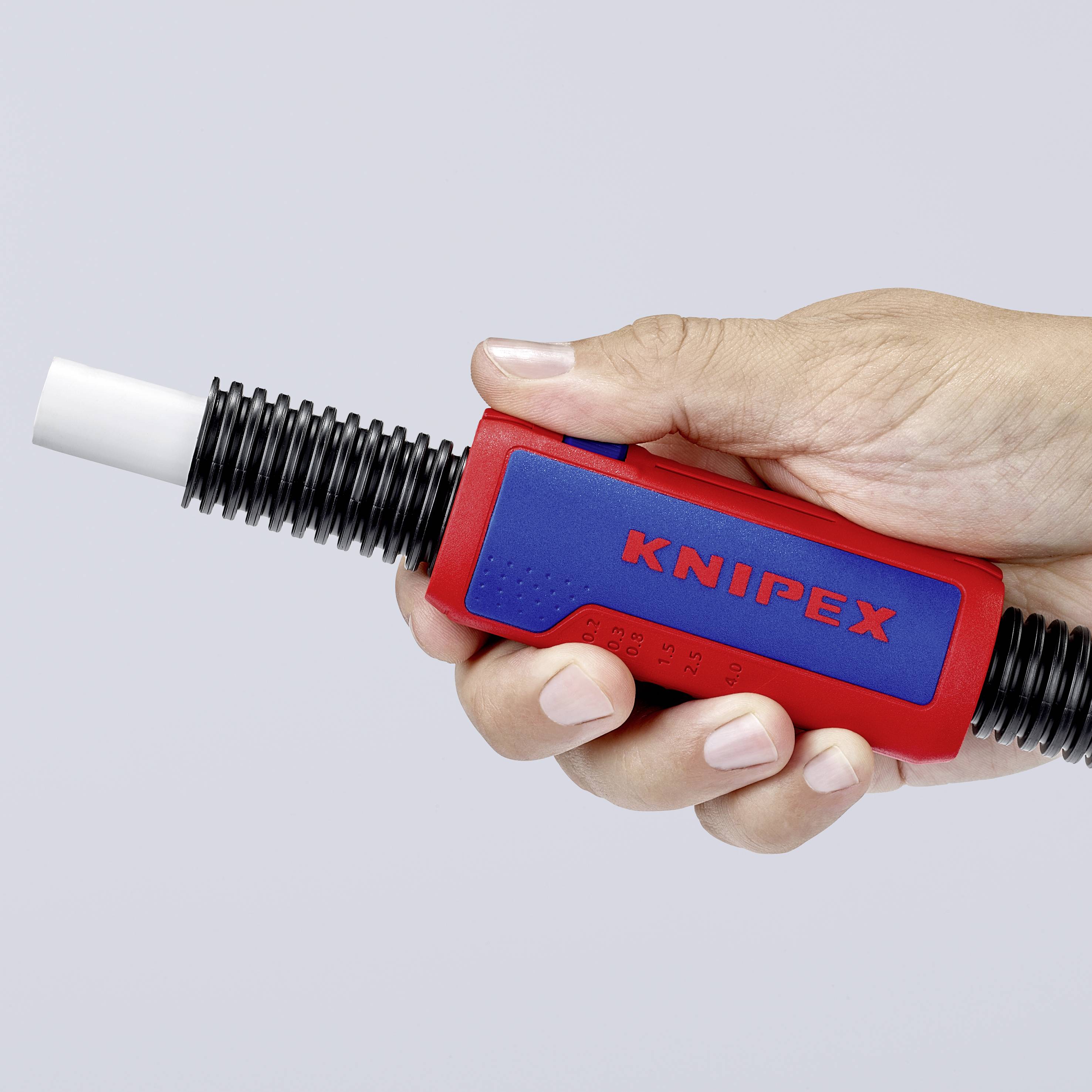 Egy kéz egy piros KNIPEX típusú kábelcsupaszítót tart. A szerszámnak fekete műanyag hegye van, és kábelszerelési munkákhoz használják.