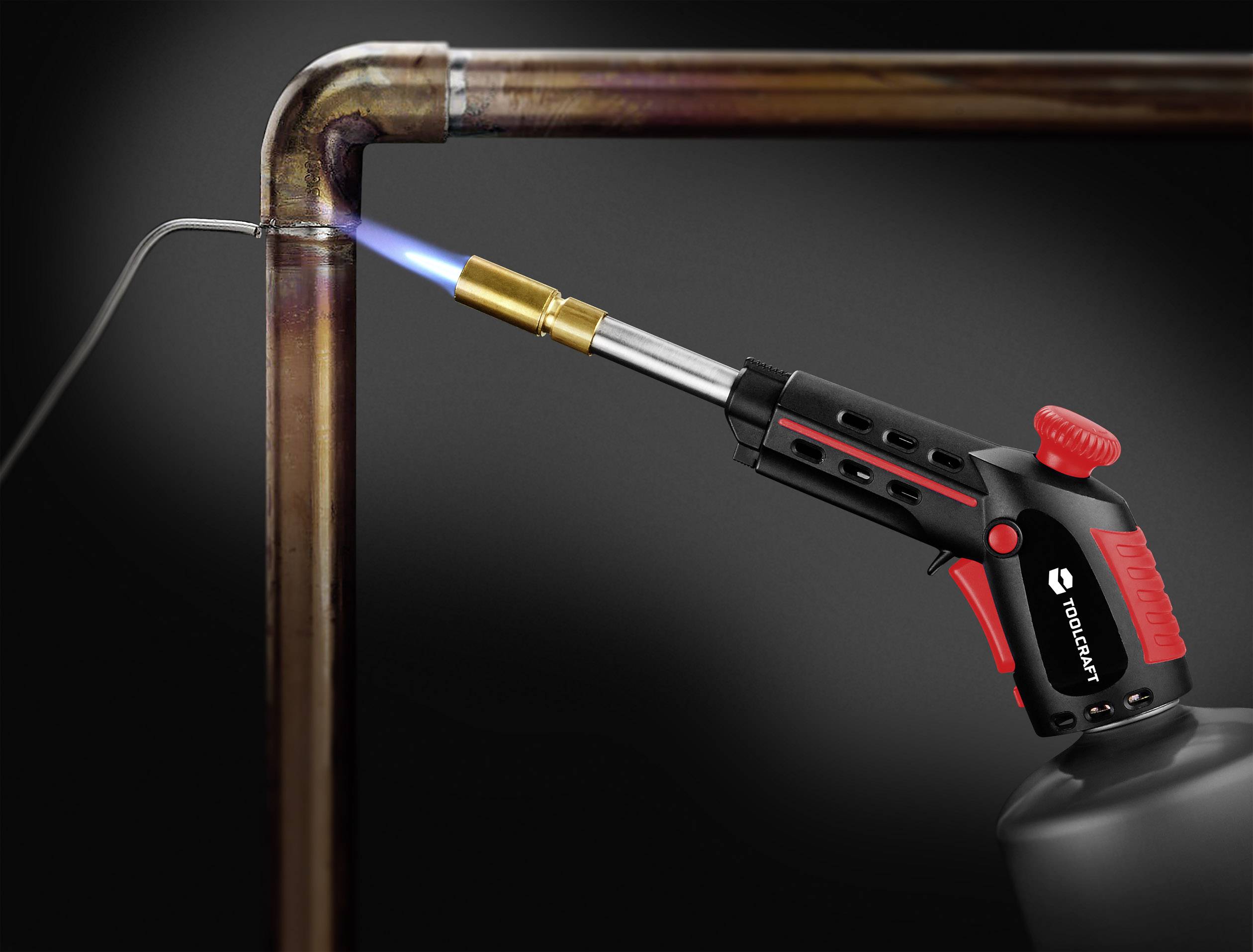 Egy forrasztólámpa hevíti a rézcsövet, hogy forrasztással összekapcsolja. A kékes láng világosan látható.