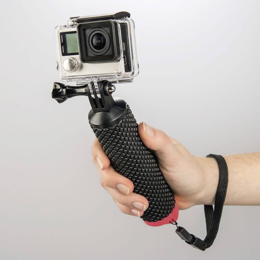 Egy kéz egy fekete fogantyúval és csuklópánttal ellátott GoPro kamerát tart, felvételre készen.