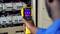 Egy személy hőkamerát használ elektromos kapcsolószekrények forró pontjainak ellenőrzésére. A képernyő több színes pontot mutat.